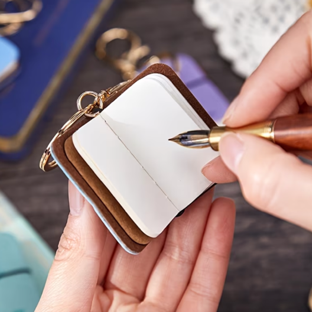 Brown mini notebook keychain charm with gold ring and clasp, open cover visible