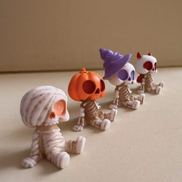Halloween skeleton figurines in mummy outfits, one with orange pumpkin head, one in purple hat