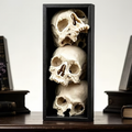 Black rectangular book end with three stacked white skull sculptures