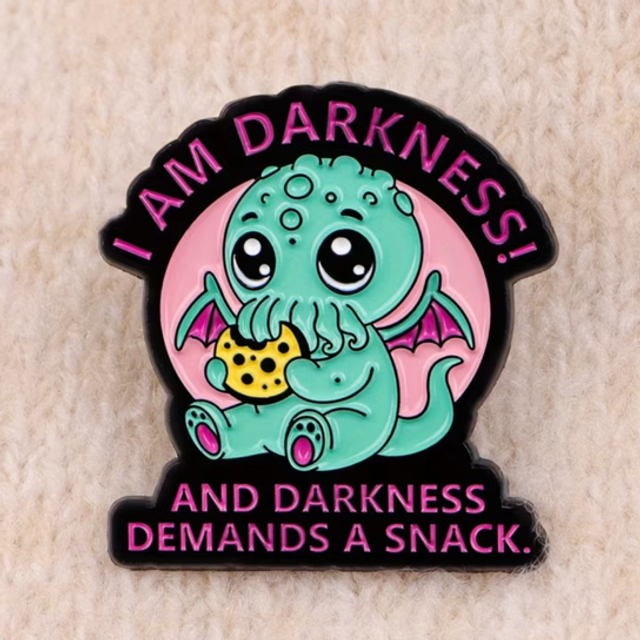 Round enamel snack pin with teal monster holding a snack, text 'I AM DARKNESS'.